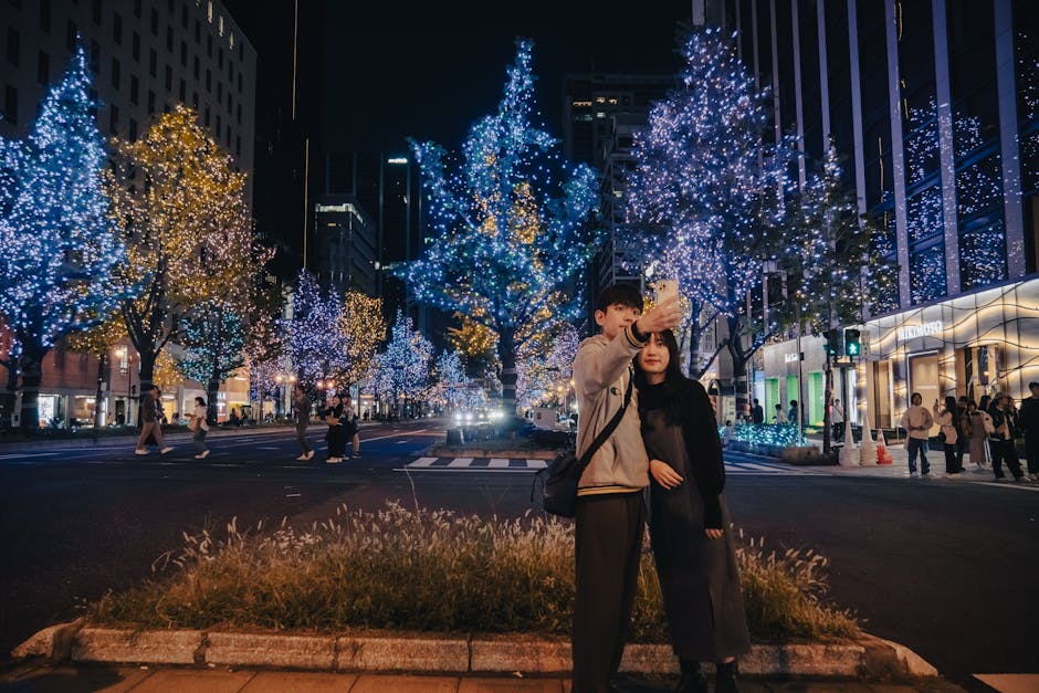 日本の大阪にある、祭りのイルミネーションに囲まれた活気に満ちた通りで、カップルが自撮り写真を撮っています。