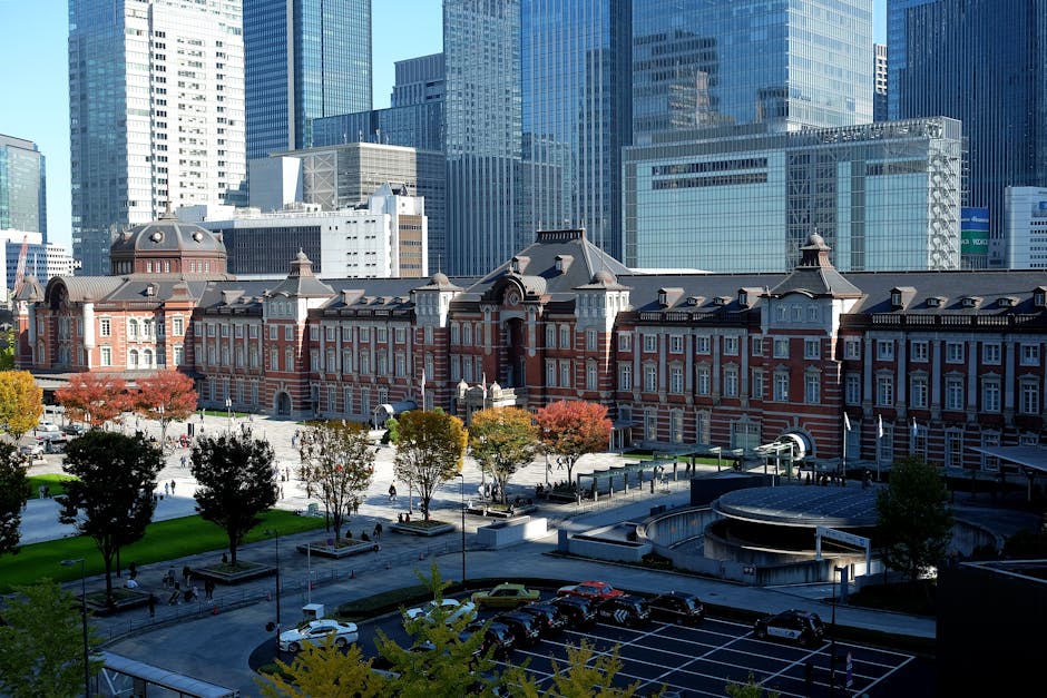 日本の東京都中央区にある、近代的な高層ビル群を背景にした東京駅と色鮮やかな紅葉。