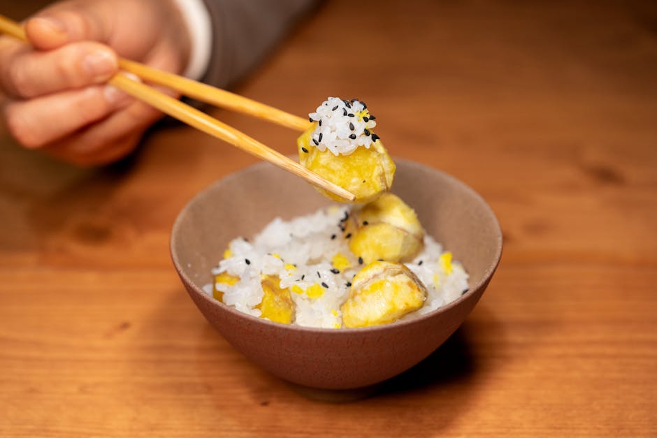 室内で、箸を使って野菜入りのご飯をすくっている様子をクローズアップで撮影した写真。