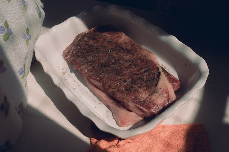 霜降りの生牛肉ステーキに味付けをし、オーブン皿に入れて自然光を捉えている。