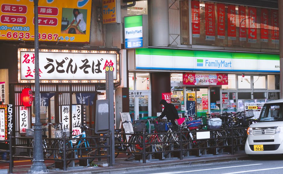 ファミリーマートとうどん屋があり、その前に自転車が停まっている日本の街並み。